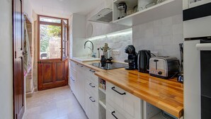 Een smalle keuken met witte kasten, een houten aanrechtblad en een uitzicht op buiten door een deur.