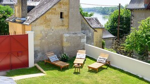 Een achtertuin met een rood hek, houten lounge stoelen, een kleine tafel en uitzicht op een rivier.