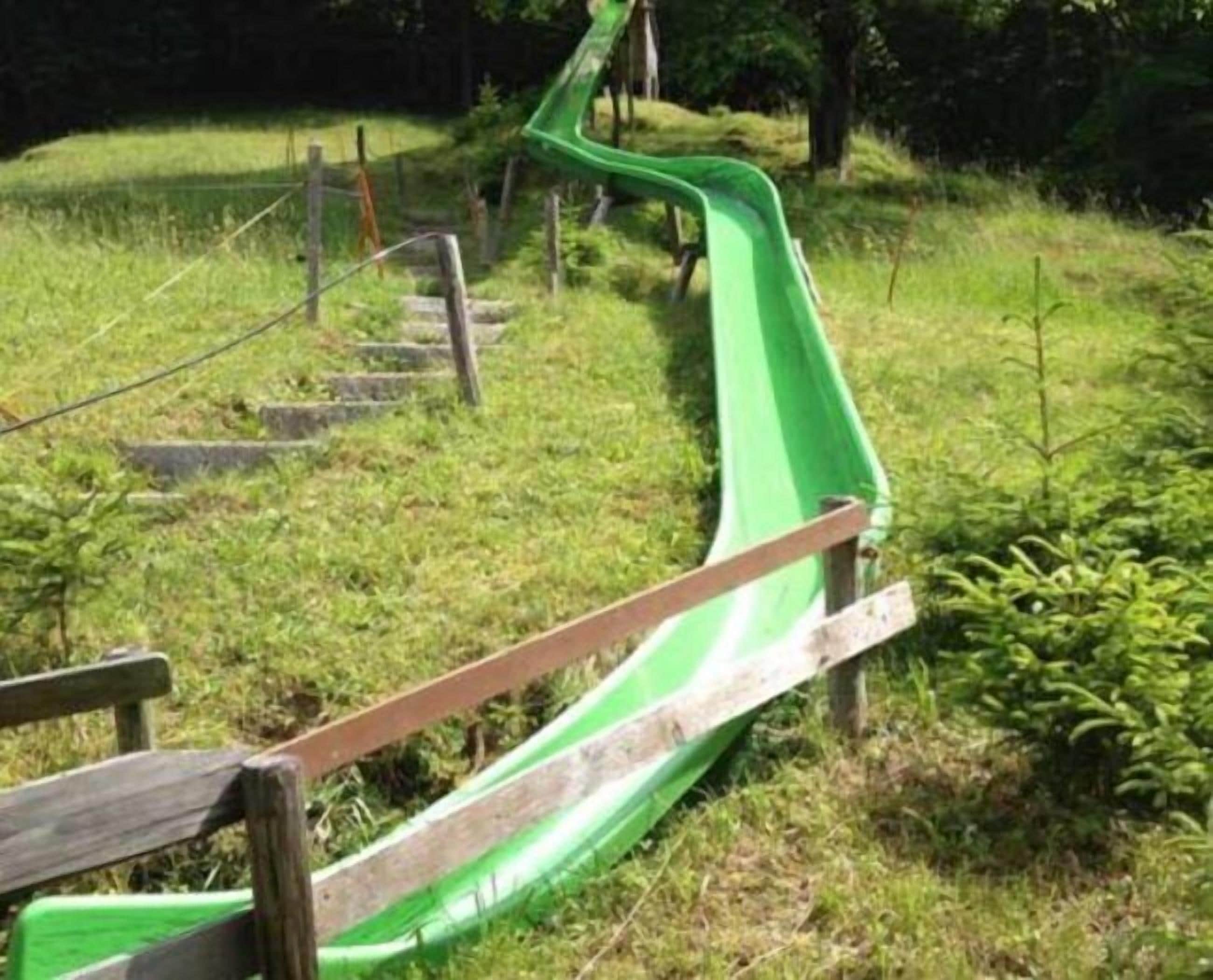 Uno scivolo verde in una zona erbosa, con una scalinata di legno che porta verso l'alto.