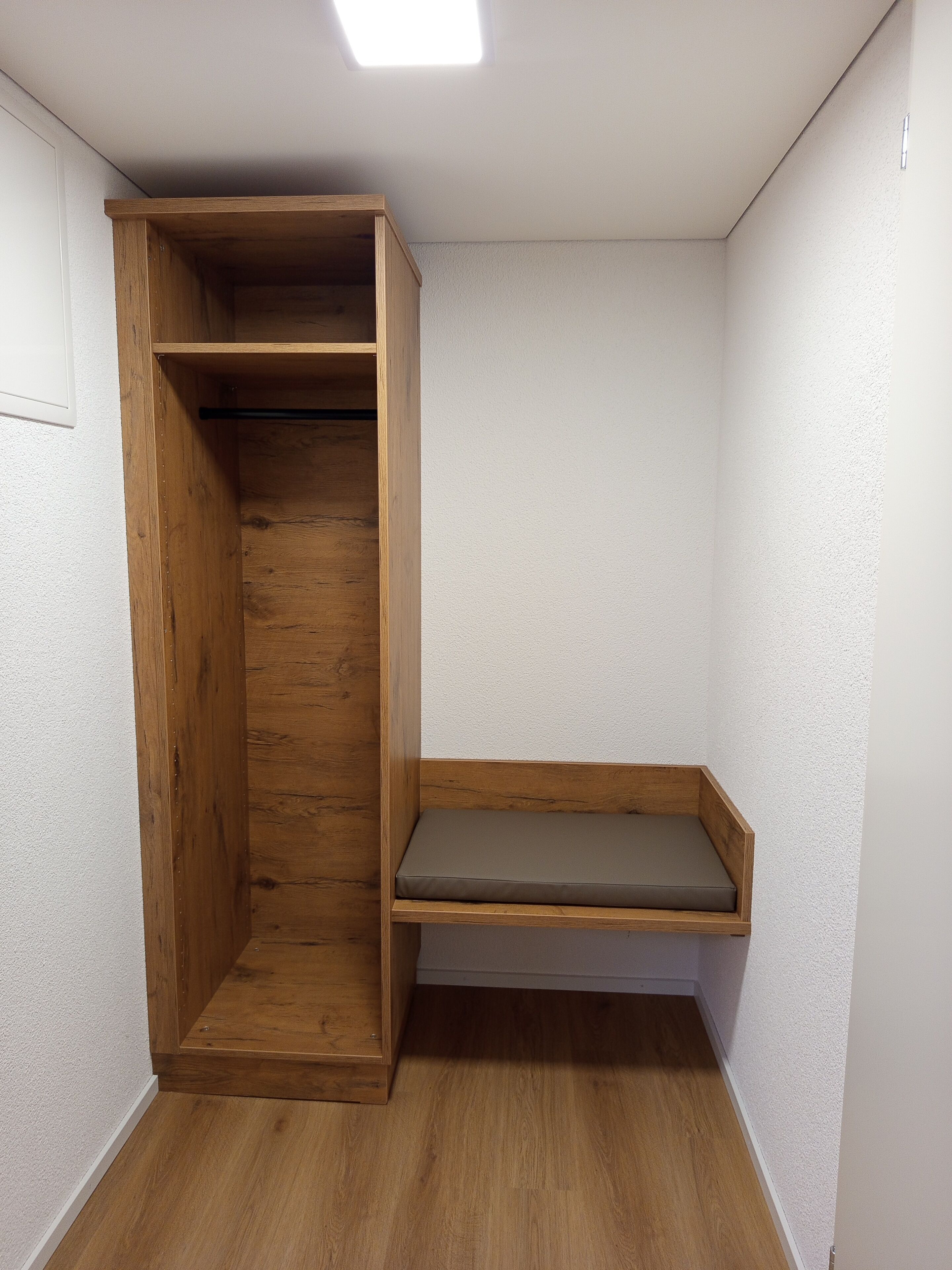 A corner room with a wooden bench and a built-in bench with a cushion.