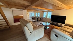 A spacious living room with a wooden ceiling, a large flat-screen TV, and a dining area in the background. - Gästehaus Rossfall 424 - Self-Check-in (Urnaesch)