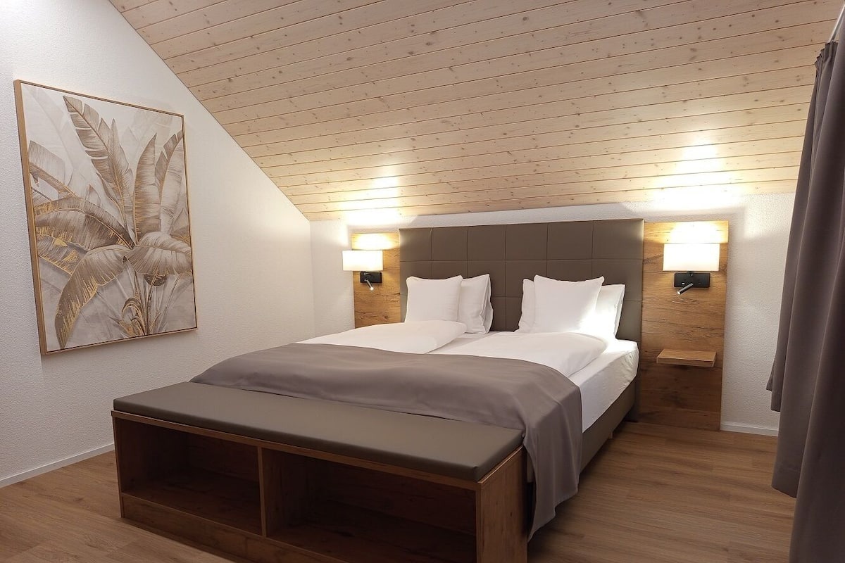 Una camera da letto con un letto, lampade sui comodini, una panca e un'opera d'arte appesa al muro.