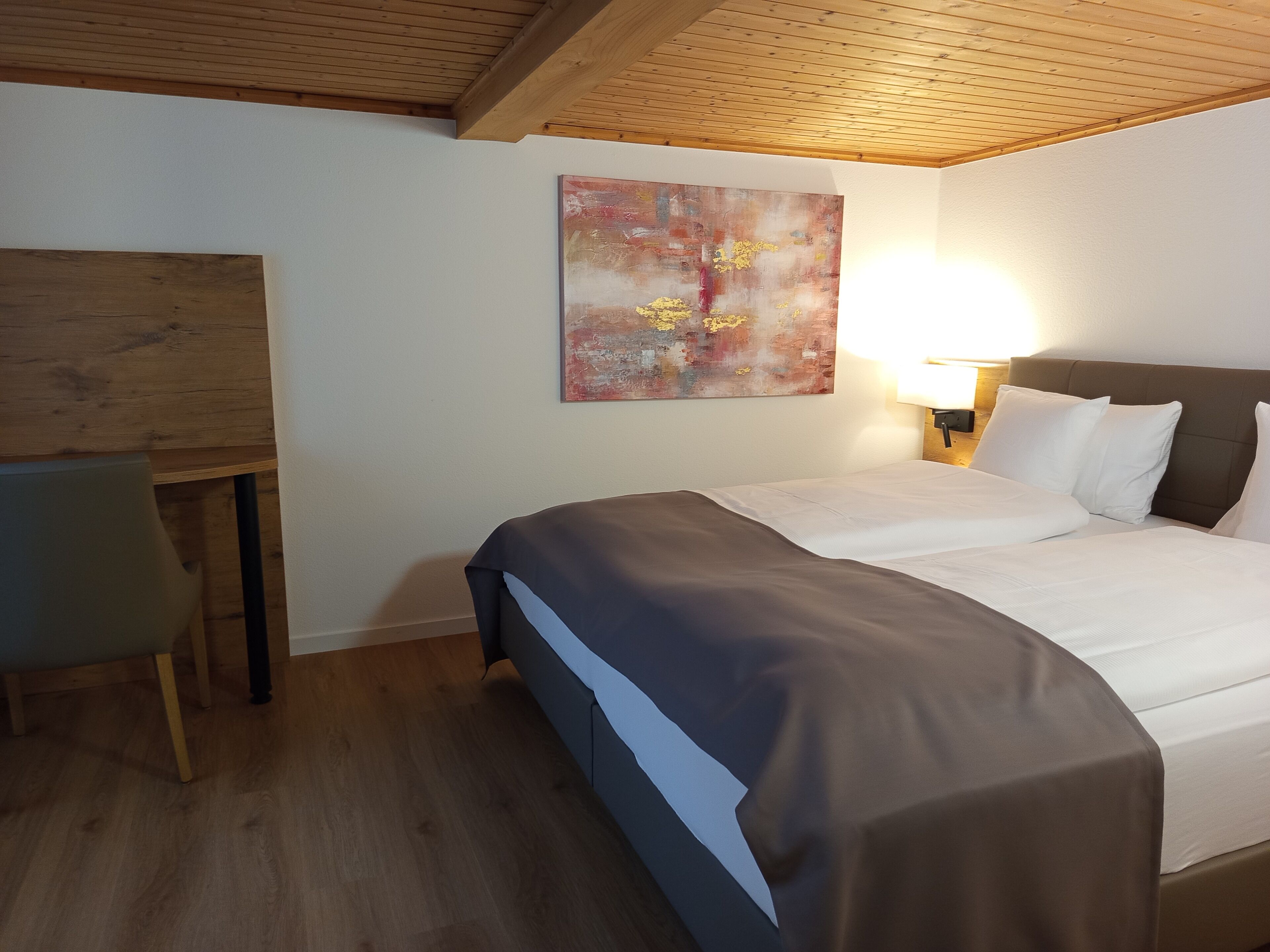 A hotel room with a bed, a desk, a chair, a lamp, and a painting on the wall.