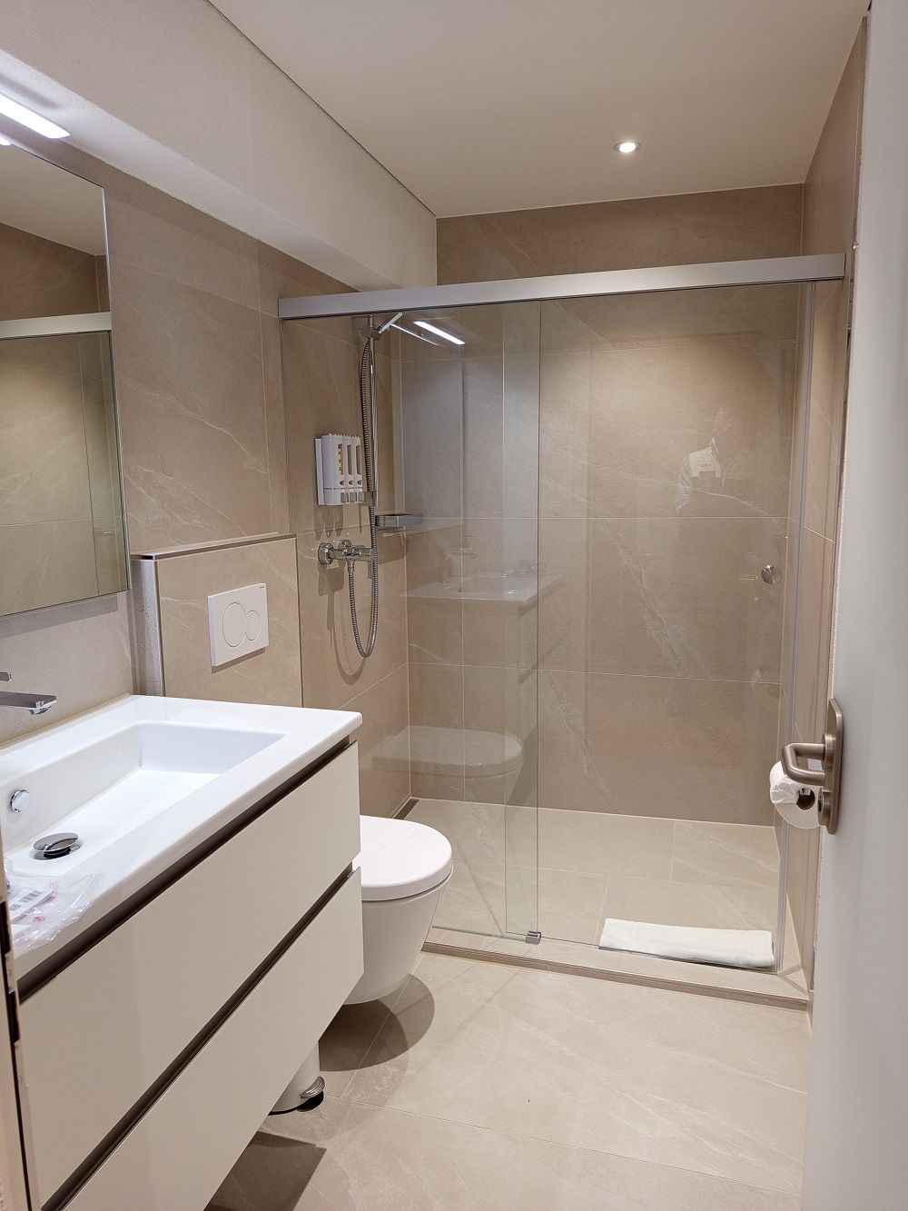 Un baño moderno con ducha de vidrio, un lavamanos blanco y un inodoro.