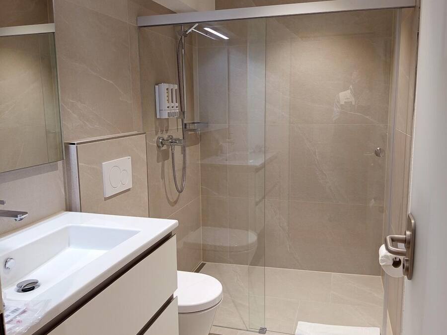 Un baño moderno con ducha de vidrio, un lavamanos blanco y un inodoro.
