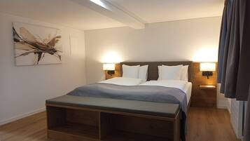 Una habitación de hotel moderna con una cama grande, lámparas de noche, un banco de madera y una obra de arte en la pared.