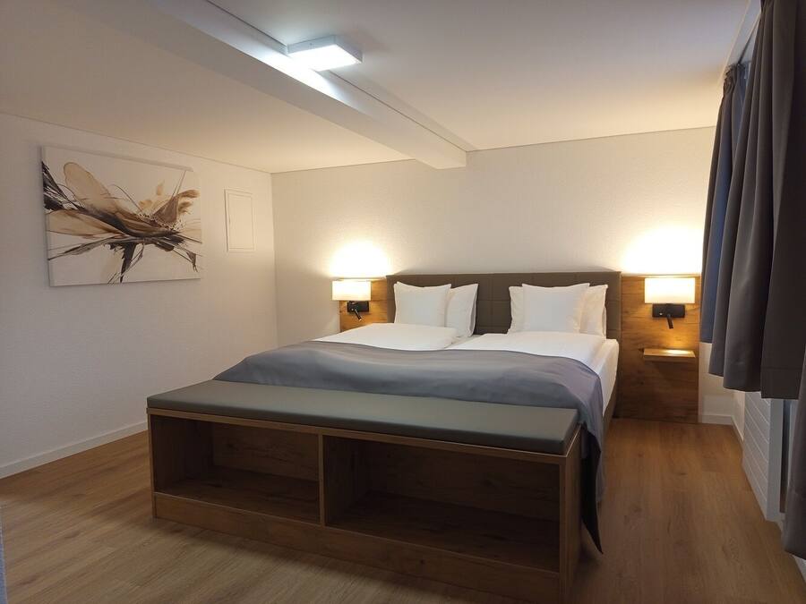 Una habitación de hotel moderna con una cama grande, lámparas de noche, un banco de madera y una obra de arte en la pared.