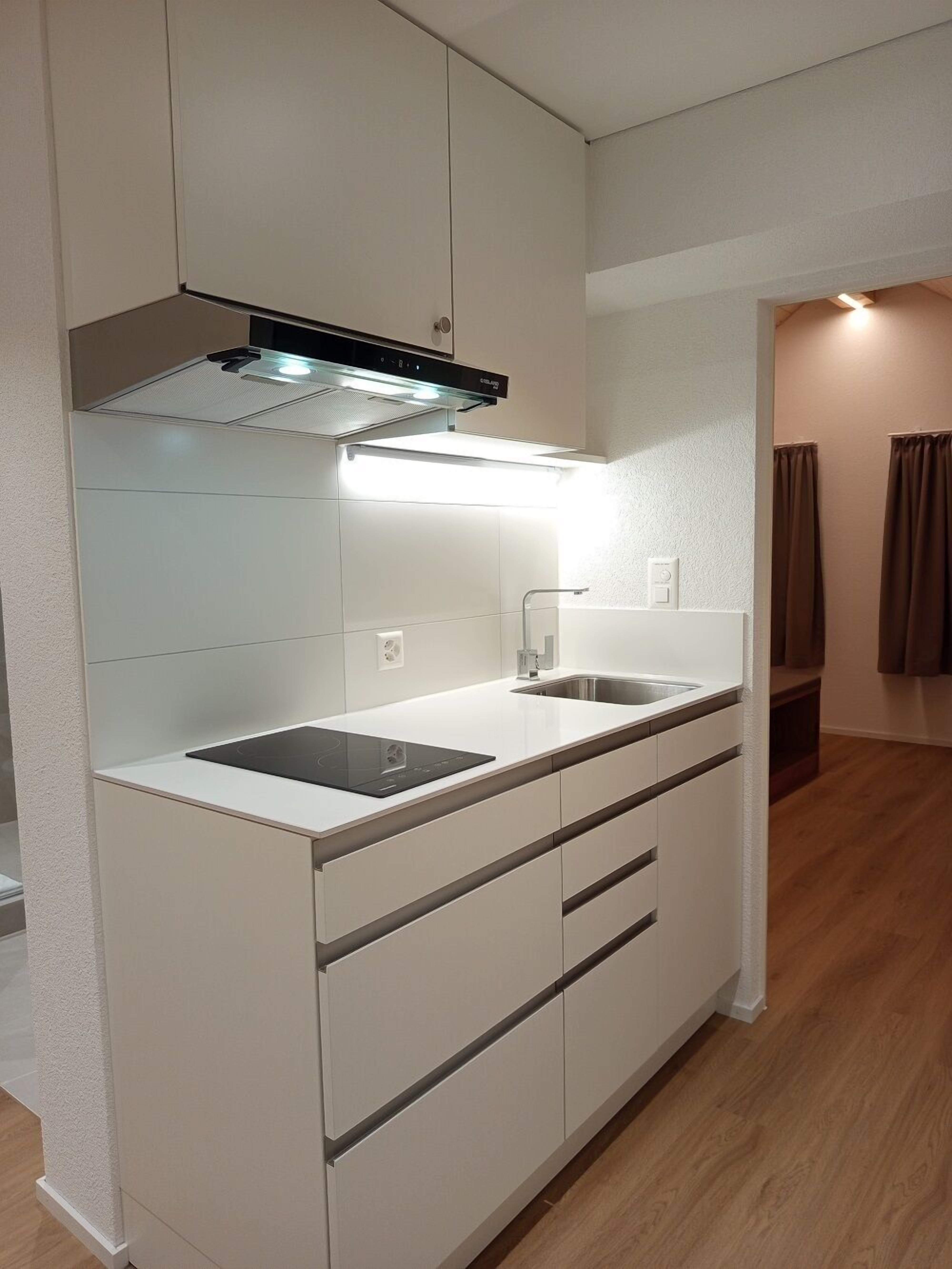 Una cocina moderna con armarios blancos, un lavamanos de acero inoxidable y una campana extractora integrada.