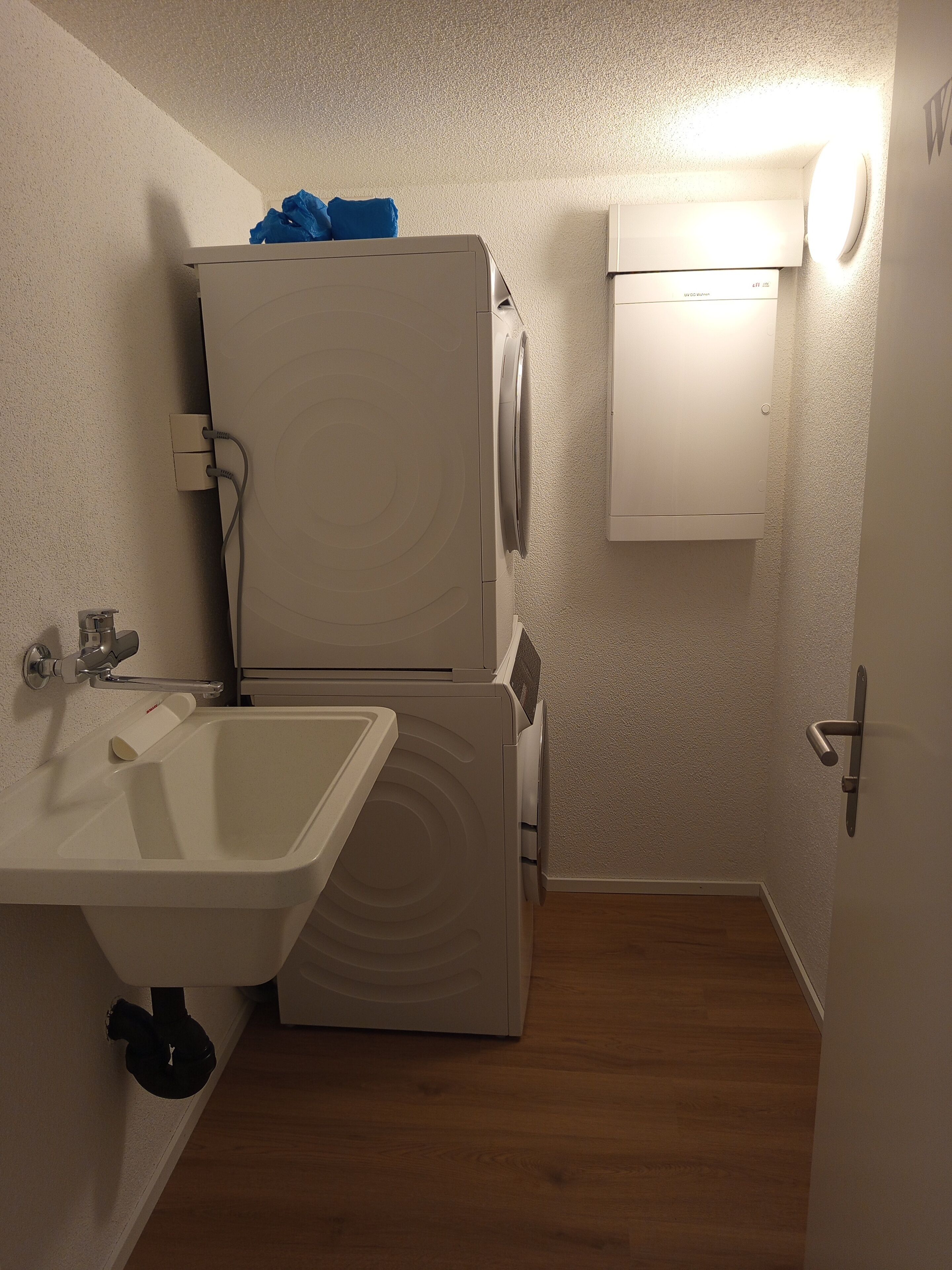 Un baño compacto con lavamanos, lavadora y secadora apiladas, y un mueble pequeño.