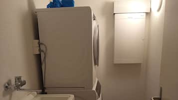 Un baño compacto con lavamanos, lavadora y secadora apiladas, y un mueble pequeño.