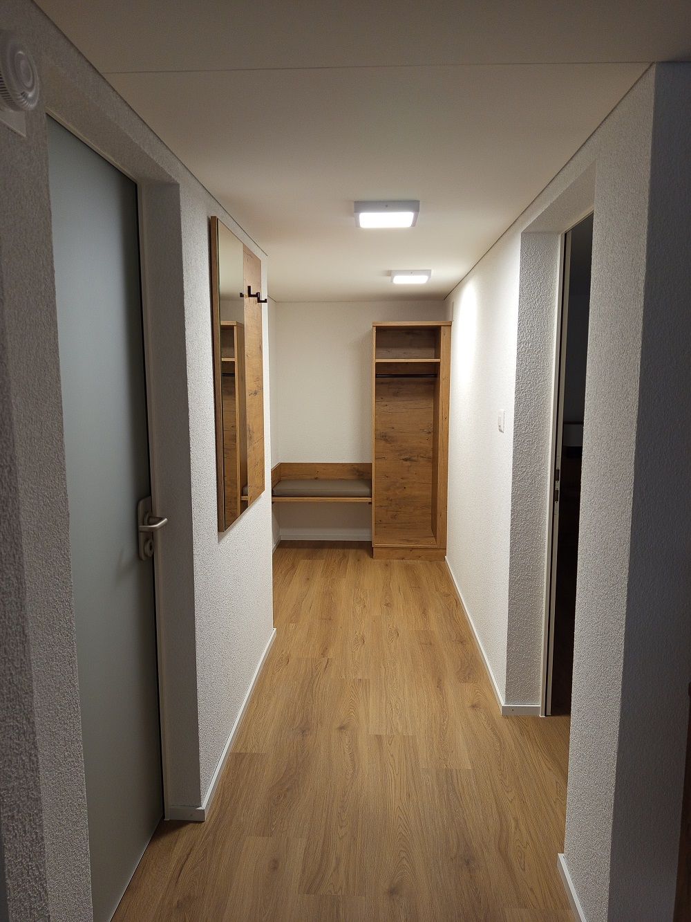 A hallway with wooden flooring, white walls, and a ceiling light.