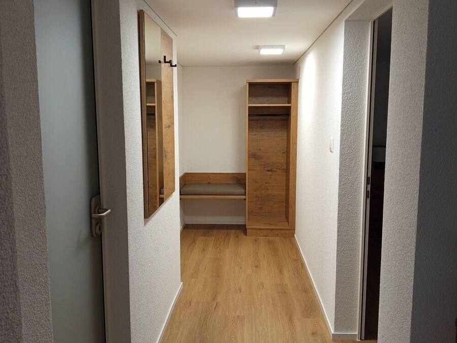 A hallway with wooden flooring, white walls, and a ceiling light.