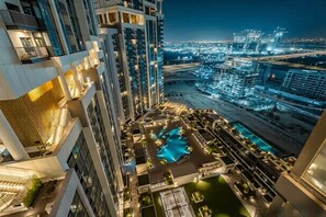 A high-rise hotel with multiple balconies, a rooftop pool, and a view of the cityscape at night.