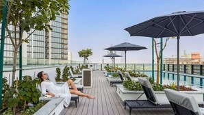 Eine Dachterrasse mit Liegestühlen, Sonnenschirmen und einem Pool.