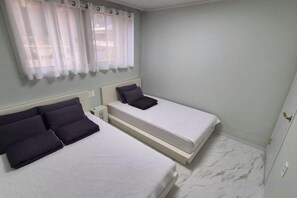 Habitación de hotel con dos camas, una mesita de noche y un ventanal con cortinas.