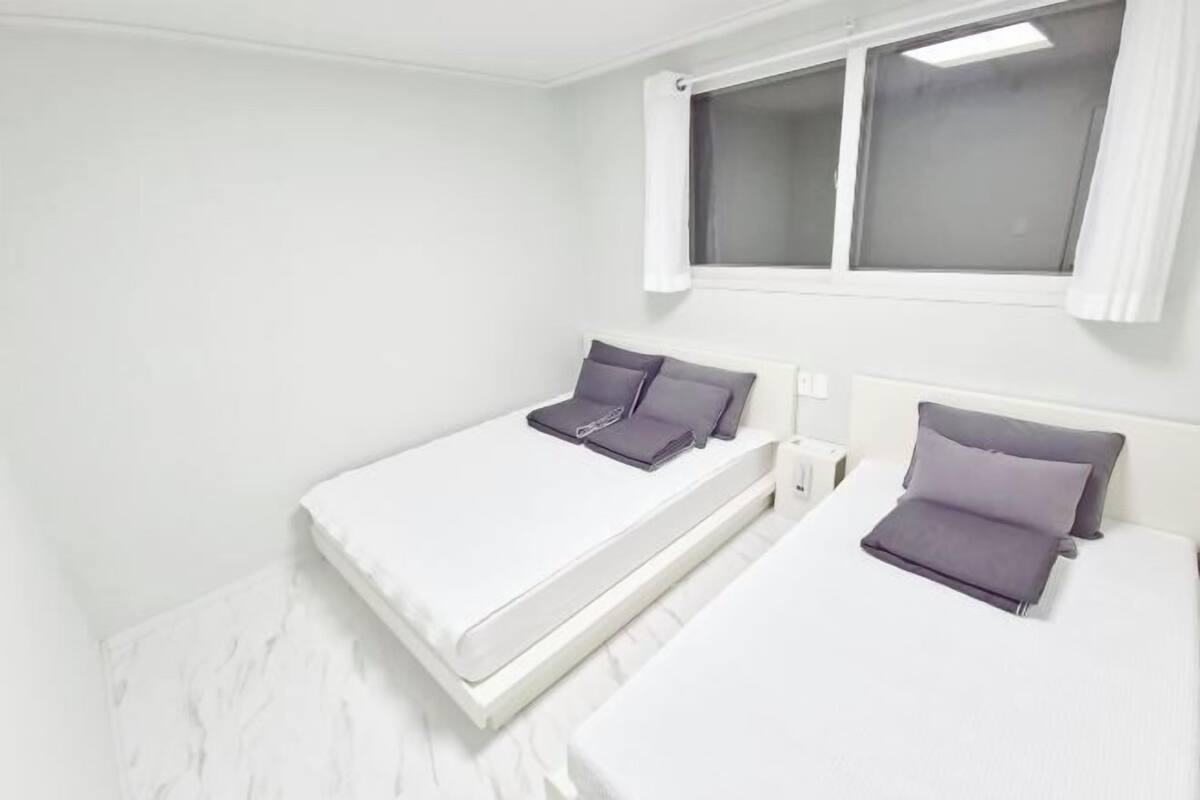 A clean, white room with two beds, each with a headboard and pillows.