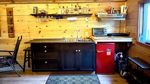 A compact kitchen with wooden walls, a black and red refrigerator, a sink, a toaster, and various kitchen utensils. - Unique cabin perched high with white pine trees (Mansfield-et-Pontefract)