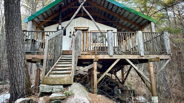 A rustic cabin with a wooden deck, a staircase, and a green roof. - Unique cabin perched high with white pine trees (Mansfield-et-Pontefract)