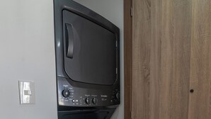 Une petite buanderie équipée d’un lave-linge et d’un sèche-linge à chargement frontal, d’une porte en bois et d’un interrupteur sur le mur.
