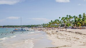 Une plage avec un bateau, des palmiers et des vacanciers.
