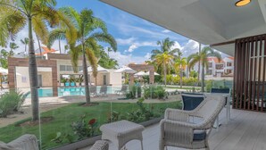 Un balcon agrémenté de meubles en osier, une piscine et des palmiers.