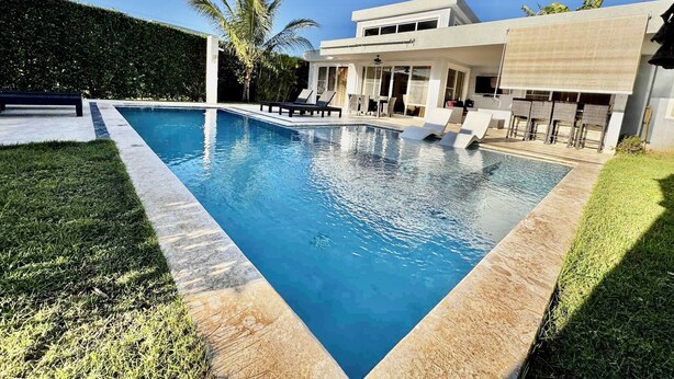 Una casa moderna con piscina, un patio con sillones de descanso y un césped bien cuidado.