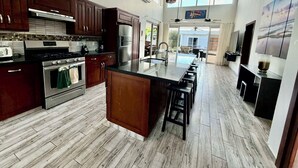 Una cocina moderna con armarios de madera oscura, electrodomésticos de acero inoxidable, una isla central con taburetes y un amplio ventanal que proporciona luz natural.