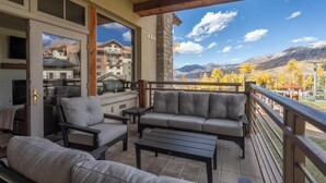 A balcony with outdoor furniture, a stone wall, and a view of a mountain range.