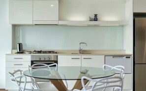 Una cucina moderna con piano cottura a gas, lavello e lavastoviglie, un tavolo rotondo in vetro e sedie bianche.