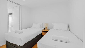 A modern hotel room with two single beds, a wooden nightstand, a lamp, and a mirror. - Q Resort on Hamilton 2 Bedroom Deluxe Hosted by Gold Coast Luxury Resorts (Surfers Paradise)