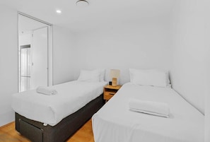 Una camera d'albergo moderna con due letti singoli, un comodino in legno, una lampada e uno specchio.