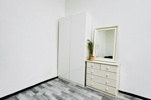Quarto com guarda-roupa branco, espelho e planta em uma cômoda.