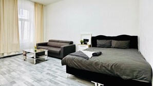 A modern bedroom with a bed, a sofa, a small table, and a nightstand.