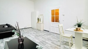 A modern room with a bed, a dining table, a chair, a vase with branches, and a door with a frosted glass panel.