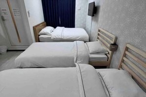 A hotel room with three single beds, a wooden headboard, a flat-screen TV mounted on the wall, and a blue curtain. - Shinkenmomotani (Osaka)