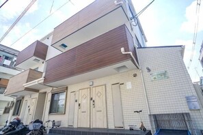Un edifici residencial de dos pisos amb façana de teules, un balcó i una entrada visible.