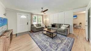 A living room with two grey sofas, a coffee table, a TV on a wooden stand, and a ceiling fan. - Big backyard hangout, firepit, large primary suite (Sarasota)