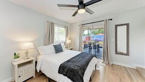 A bedroom with a bed, bedside tables, a ceiling fan, and a view of an outdoor area. - Big backyard hangout, firepit, large primary suite (Sarasota)