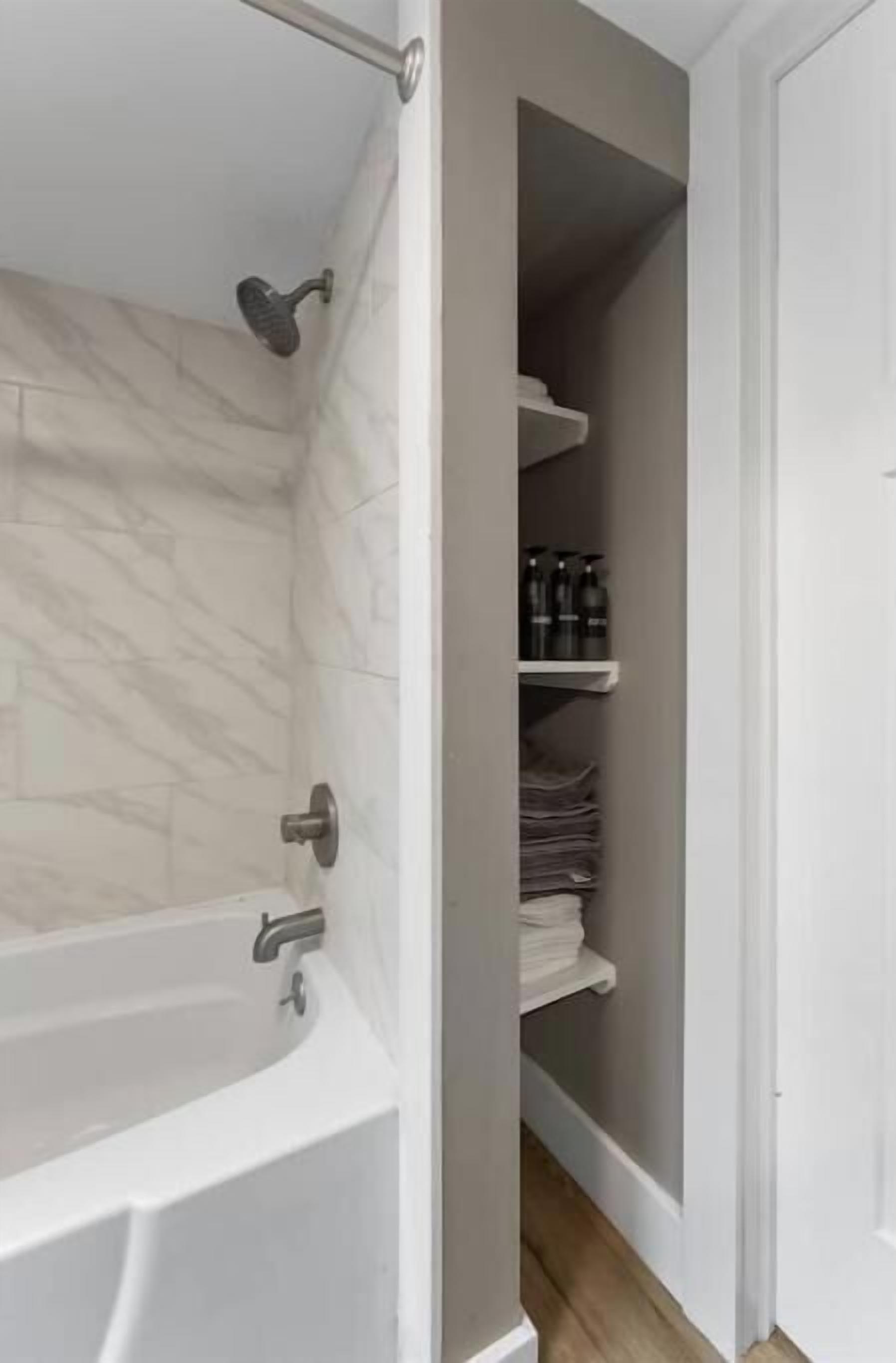 Ein Badezimmer mit einer weißen Badewanne, einer Duschbrause und einem Ablagefach mit Toilettenartikeln.