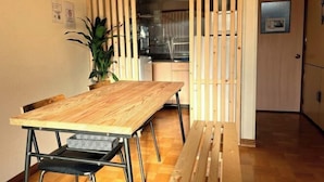 A dining area with a wooden table and chairs, a kitchen in the background, and a sliding door. - City Yugawa Room D (Hakodate)