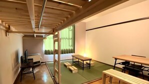 A room with a wooden ceiling, a green tatami mat floor, a wooden table, a bench, and a futon bed. - City Yugawa Room D (Hakodate)