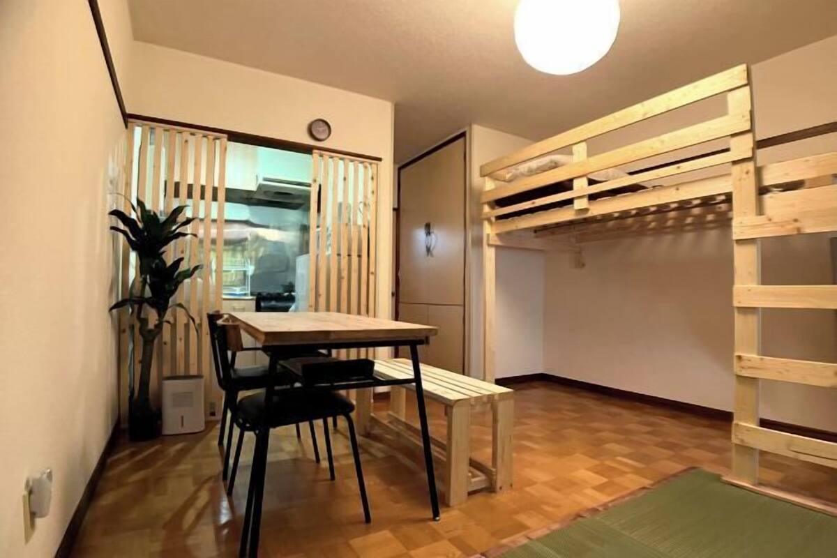 A compact room with a wooden dining table, black chairs, a bench, a wooden bunk bed, and a potted plant.