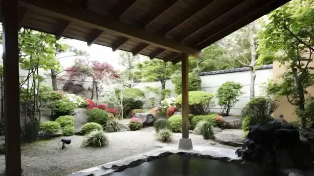 A tranquil garden with a pond, stone pathways, and various shrubs and trees. - City Yugawa Room D (Hakodate)
