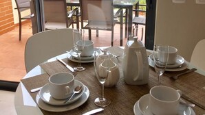 Ein Essbereich mit einem Tisch, gedeckt für zwei Personen, mit Tellern, Tassen, Besteck und einer Wasserkaraffe.