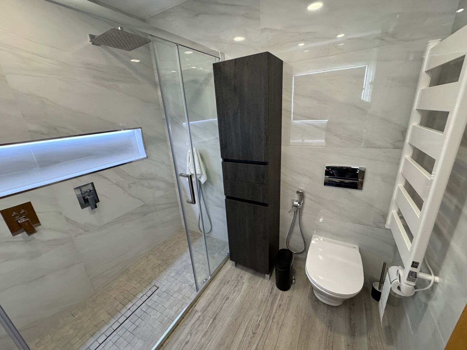 A modern bathroom with a glass shower enclosure, a toilet, and a built-in vanity with a mirror.