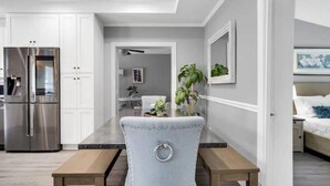 Una cocina moderna con armarios blancos, un refrigerador de acero inoxidable y una mesa de comedor de madera con una silla tapizada en azul claro.