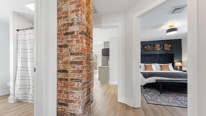 A modern hotel room with a brick accent wall, a bed with pillows, a bedside table, and a view of the hallway. - Historic Canal Retreat in Downtown Canal Fulton (Canal Fulton)