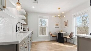 A modern kitchen with white cabinetry, a central island, and a dining area with two chairs. - Historic Canal Retreat in Downtown Canal Fulton (Canal Fulton)