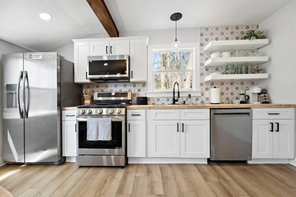 A modern kitchen with white cabinets, stainless steel appliances, and a wooden countertop.