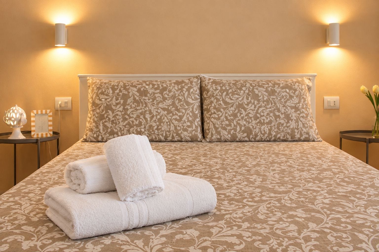 A neatly made bed with a patterned bedspread, two pillows, and folded towels.